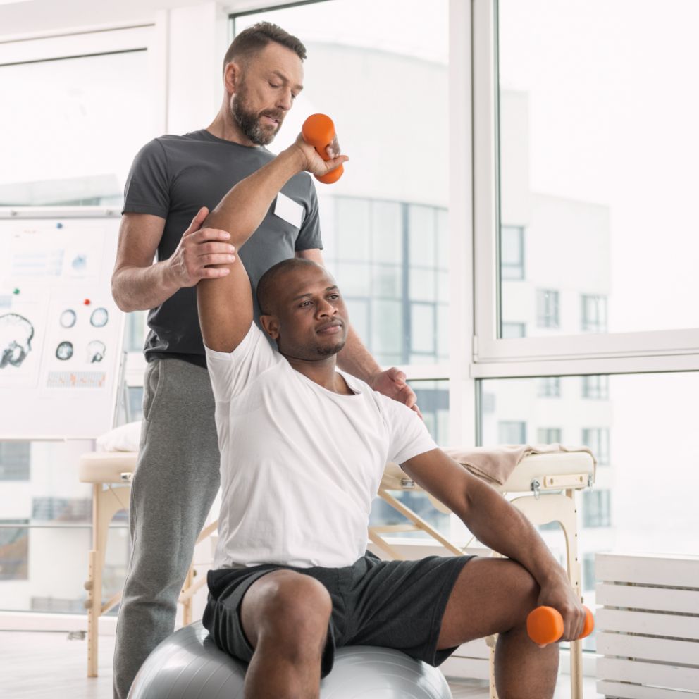 Man performing physical therapy on a man holding small orange weights